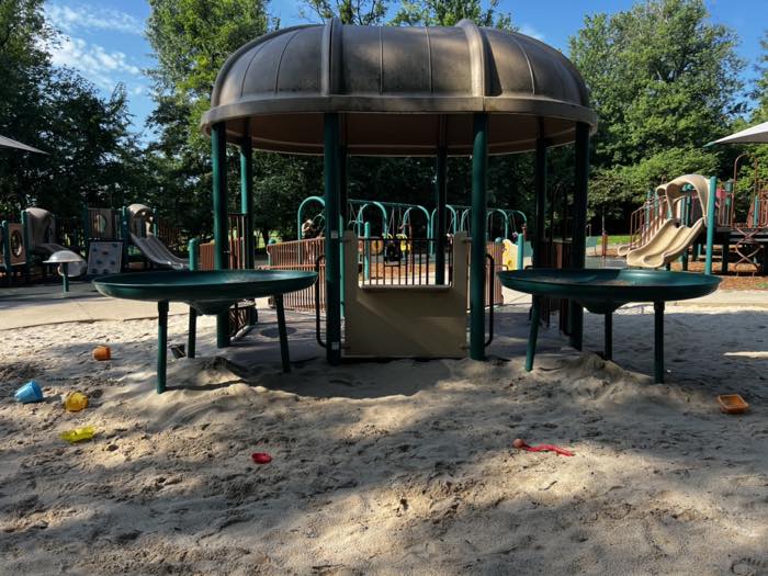 A sand play area with two large raised green sand tables on legs and a domed shelter behind them.