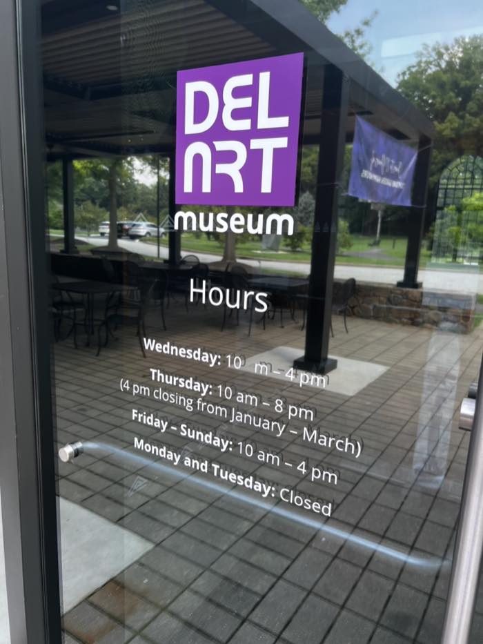 Opening hours printed in white vinyl on a glass door: Wednesday 10am to 4pm, Thursday 10am to 8pm with a 4pm closing from January to March, Friday to Sunday 10am to 4pm, Monday and Tuesday closed.